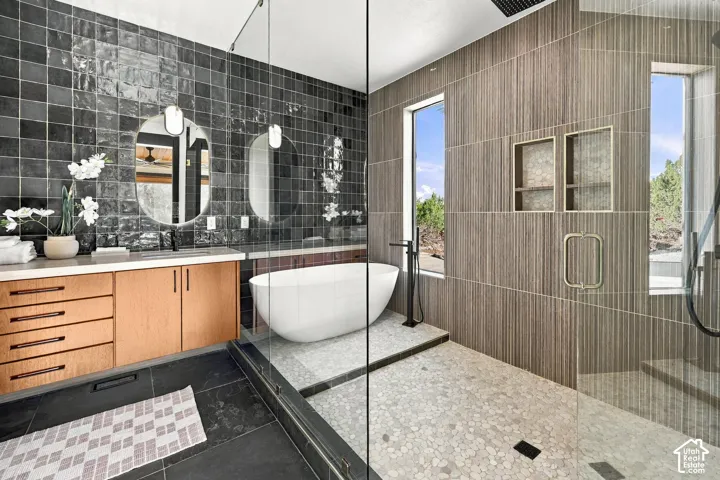 Master Ensuite featuring a floating vanity with a light wood finish, a freestanding oval soaking tub, a walk-in shower with pebble-stone flooring, and charcoal-toned ceramic wall tile