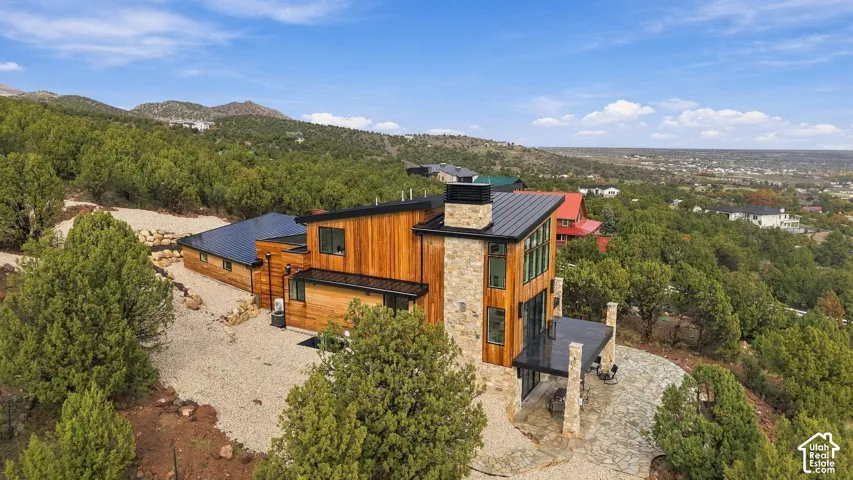 Contemporary multi-level residence featuring vertical wood siding, a standing-seam metal roof, a natural stone chimney, and a stone-paved patio