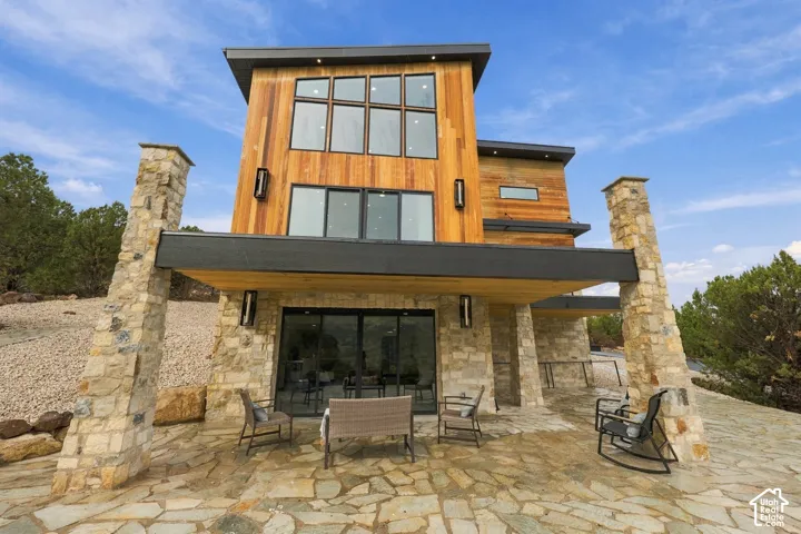 Multi-level contemporary exterior featuring vertical wood siding, expansive multi-pane windows, stone-clad structural pillars, and a flagstone patio