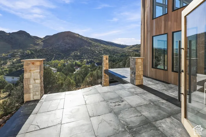 Master bedroom outdoor deck, featuring large-format slate flooring, stacked stone columns, wood-clad siding, and expansive mountain scenery
