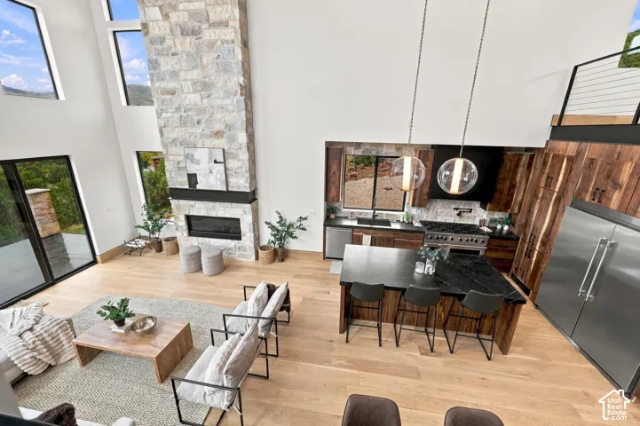 Double-height living area featuring a full-height stone-clad fireplace, light-tone wood flooring, gourmet kitchen with a contrasting dark stone island, and large-format sliding glass doors