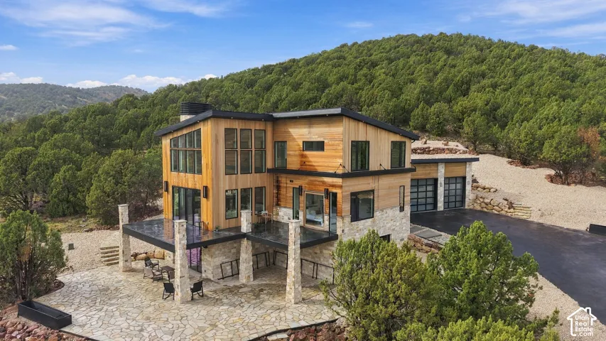 Modern multi-level exterior featuring natural wood siding, stone veneer accents, large-scale glass windows, a covered stone patio, and a two-car garage
