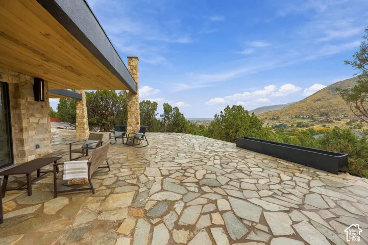 Flagstone patio featuring stacked-stone pillars, wood-finished ceiling soffits, and a linear built-in planter, set against a mountainous landscape