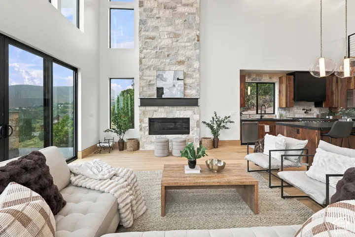 Double-height ceilings, floor-to-ceiling stone fireplace with a metal mantel, wood-finish flooring, and expansive windows
