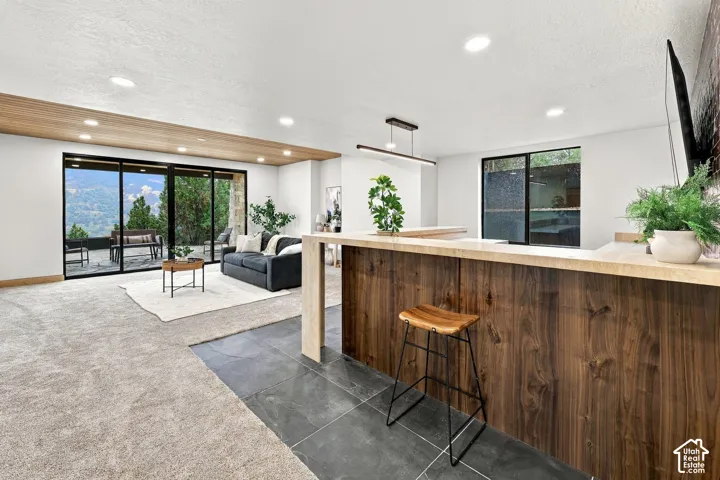 Open-concept area featuring floor-to-ceiling glass sliding doors, wood-finish ceiling accent, linear pendant lighting, large-format tile flooring, and a built-in bar with wood-grain cabinetry