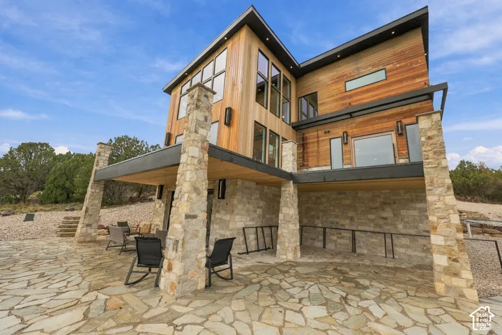Contemporary multi-level exterior featuring wood-paneled siding, stone veneer accents, structural stone pillars, and oversized windows