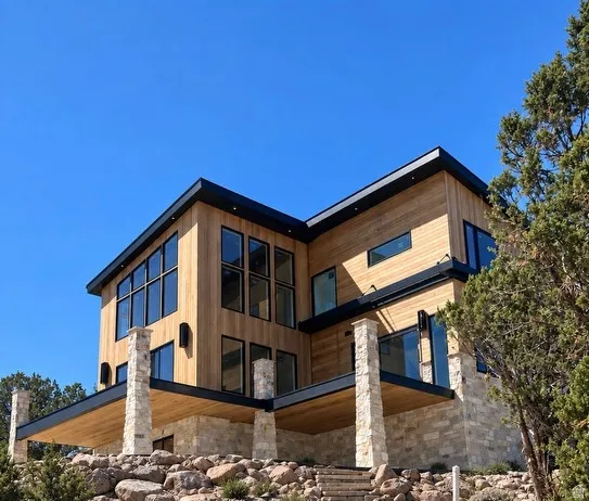 Contemporary exterior featuring wood siding, extensive black-framed windows, a flat roofline, and stone-clad foundational elements