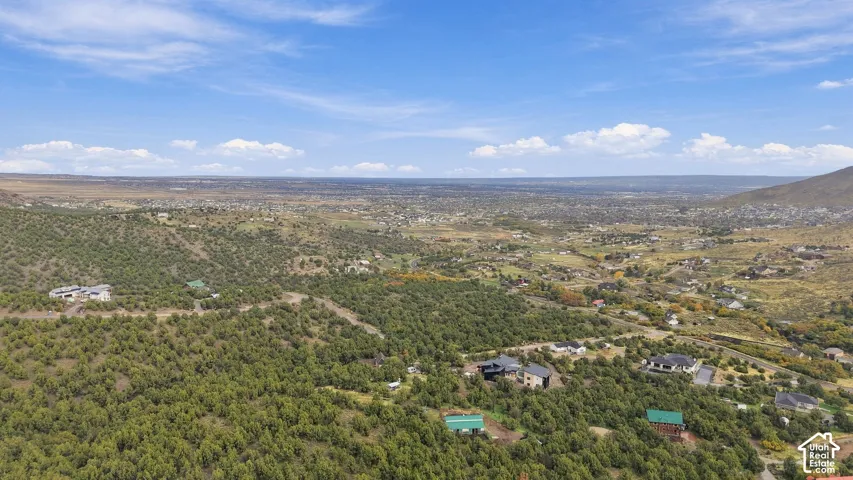 Aerial perspective featuring high-elevation terrain, native scrub vegetation, expansive mountain backdrop, and scattered residential development