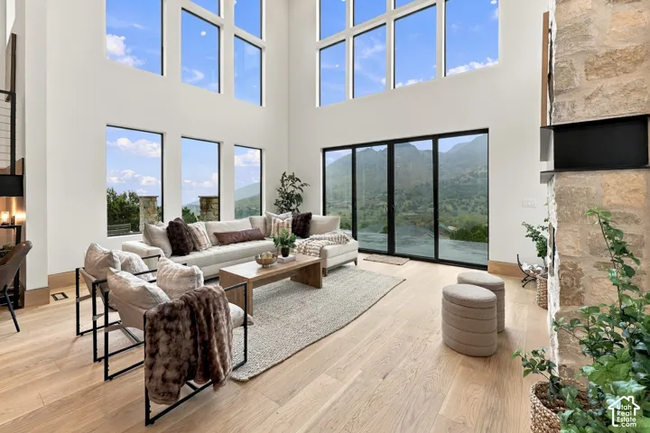 Double-height ceilings with expansive multi-pane windows, wood-finish flooring, full-height stone fireplace surround, and black-framed sliding glass doors