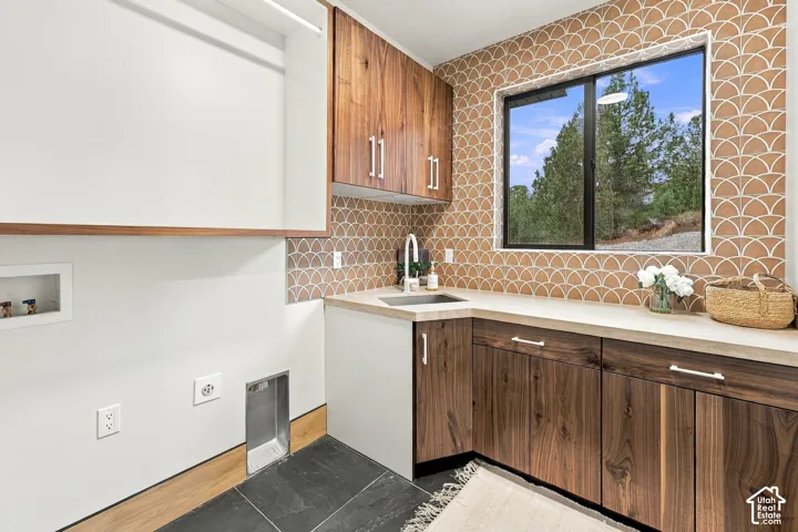 Utility area featuring custom wood-finish cabinetry, a drop-in sink with a high-arch faucet, a stone-composite countertop, and scalloped tile backsplash