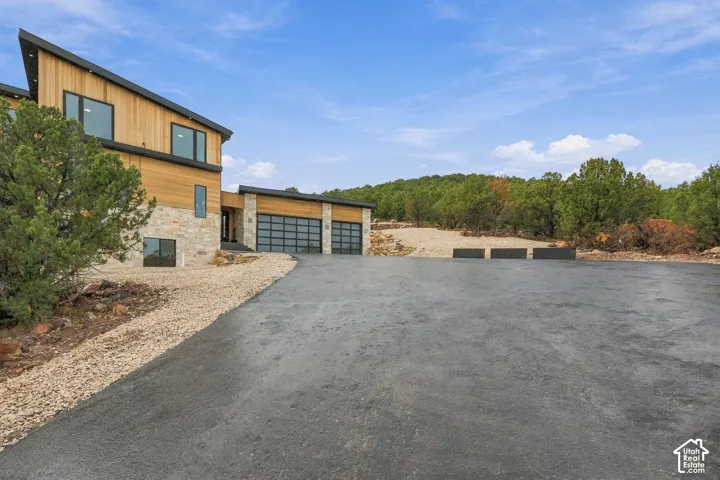 Modern exterior featuring wood siding, natural stone accents, a shed roofline, and a multi-car garage with glass-paneled doors