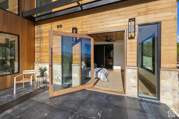 Master Private Deck with wood siding, stone lower cladding, a pivoting glass door, large-format dark stone patio tiles, and black metal wall-mounted lighting