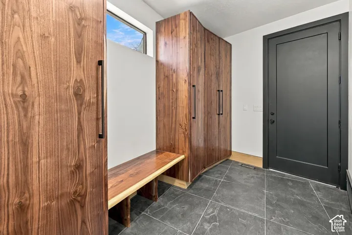 Built-in wood-finish cabinetry, matching live-edge bench, matte black hardware, dark stone-tile flooring, and solid-core black door