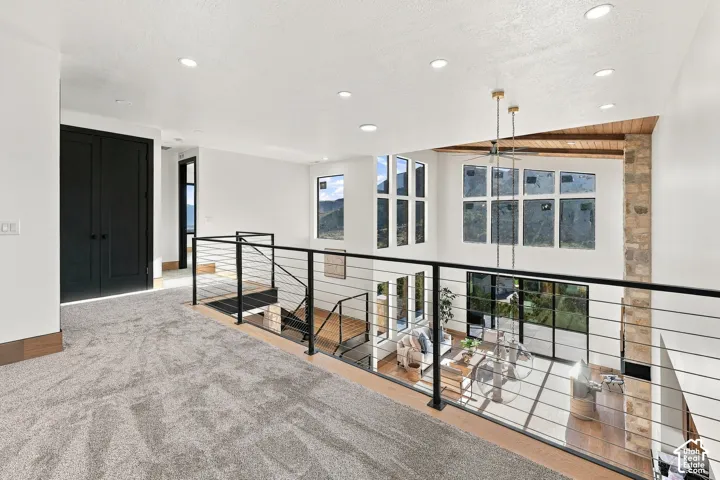 Open loft area featuring recessed lighting, a black metal cable railing system, carpeted flooring, and a natural stone chimney breast with vaulted timber ceiling beams