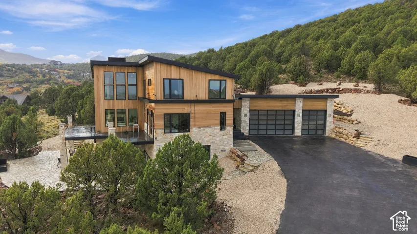 Modern exterior featuring wood siding, natural stone accents, shed roofline, multi-pane windows, and a three-car garage with glass panel doors