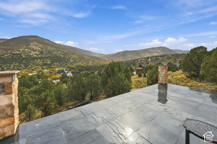 Master bedroom outdoor terrace with elevated stone patio featuring large-format dark tile flooring and integrated stone pillar accents, set against a backdrop of mountain scenery and native landscape