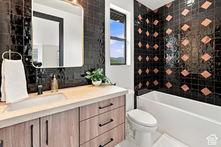 Bathroom featuring a wood-finish vanity with an integrated basin, a rounded rectangular mirror with a gold-tone frame, and high-gloss black wall tiling with a diamond-pattern accent