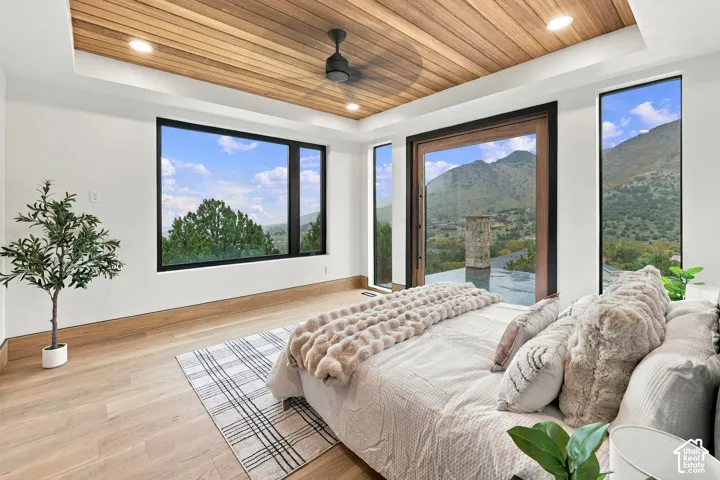 Tray ceiling with wood-plank finish and matte black ceiling fan, wood-finish flooring, floor-to-ceiling windows, and mountain scenery
