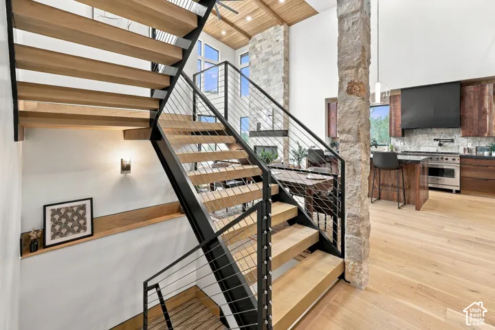 Open staircase featuring wood treads and metal cable railing, natural stone pillar, vaulted wood-plank ceiling, and wood-finish flooring