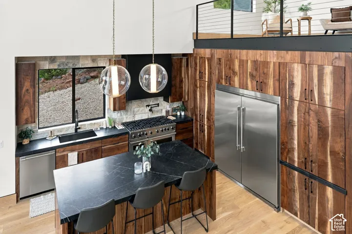 Kitchen featuring floor-to-ceiling wood cabinetry, expansive stone-topped island, professional-grade stainless steel appliances, stone backsplash, and dual globe pendant lighting