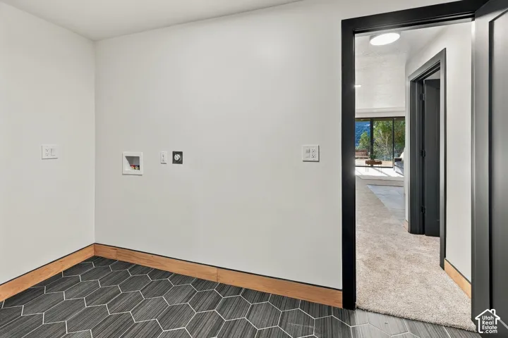 Laundry space featuring charcoal-toned hexagonal floor tile, wood trim accents, and dark-finished door casings