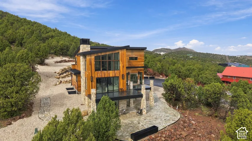 Contemporary residence featuring natural wood siding, stacked stone exterior accents, expansive floor-to-ceiling windows, a mono-pitch roofline, and a flagstone patio