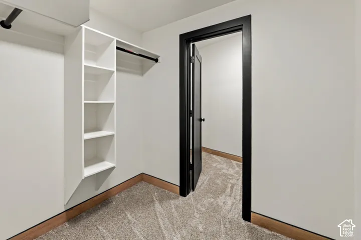 Walk-in storage space featuring custom white shelving, matte black hanging rods, neutral wall-to-wall carpeting, and a black-framed doorway