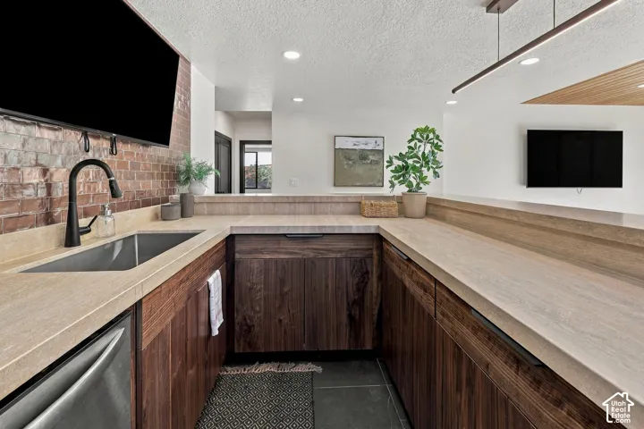 Kitchen featuring dark wood cabinetry, light-toned countertops, exposed brick wall accents, stainless steel undermount sink, and matte black pull-down faucet