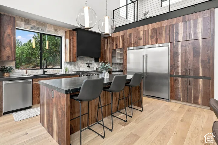 Custom wood-finish cabinetry, dark stone countertops, stainless steel appliances, stone backsplash, and wood-finish flooring