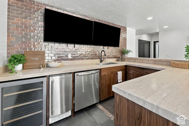 Wet bar featuring a brick-tiled backsplash, custom wood cabinetry, stone-finish countertops, stainless steel appliances, and a matte black faucet