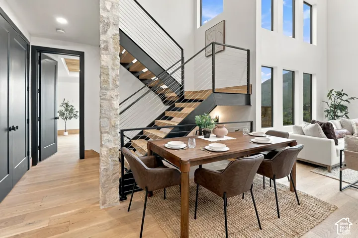 Staircase featuring wood-finish treads, a black metal frame, and cable railings, natural stone pillar, wood-finish flooring, and multi-story windows