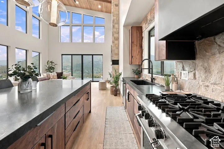 Gourmet kitchen featuring flat-panel wood cabinetry, dark stone countertops, professional-grade gas range, stone-accented wall, and wood-finish flooring beneath a vaulted ceiling with large glass windows