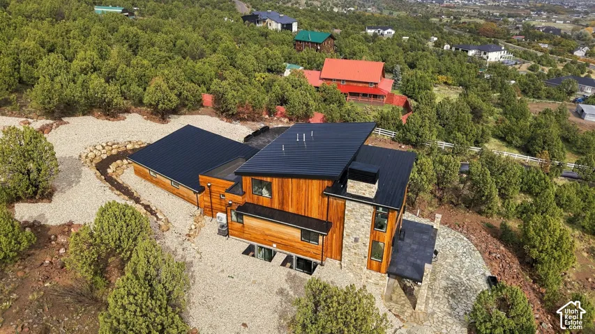 Contemporary multi-level residence featuring vertical wood siding, a standing-seam metal roof, a natural stone chimney, and an expansive stone patio