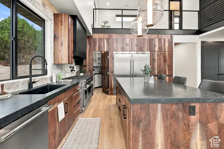 Kitchen featuring wood-finish cabinetry, a large central island with a stone countertop, wood-finish flooring, stainless steel appliances, and a metal staircase railing
