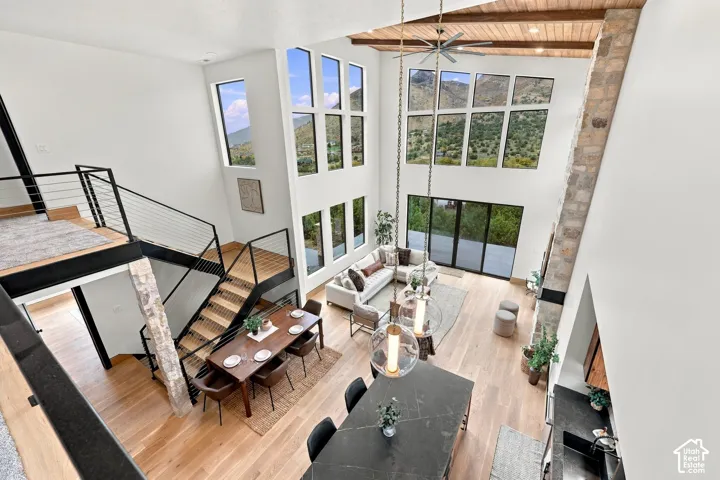 Double-height living area featuring floor-to-ceiling windows, natural stone fireplace surround, wood-plank ceiling with exposed beams, wood-finish flooring, and a floating staircase with metal railing