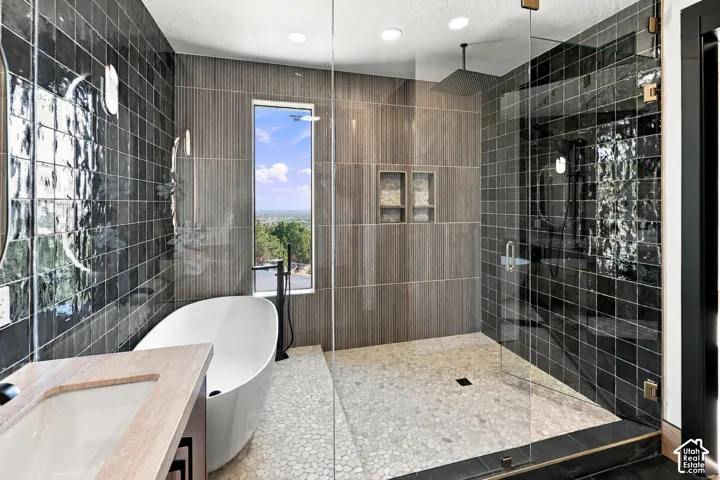 Master Ensuite with walk-in shower featuring a pebble tile floor, charcoal wall tile, built-in recessed shelving, and a glass enclosure, paired with a freestanding soaking tub and black plumbing fixtures