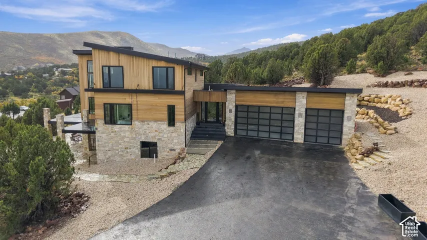 Modern multi-level exterior featuring wood siding, natural stone veneer, a shed roofline, and an attached three-car garage with glass panel doors