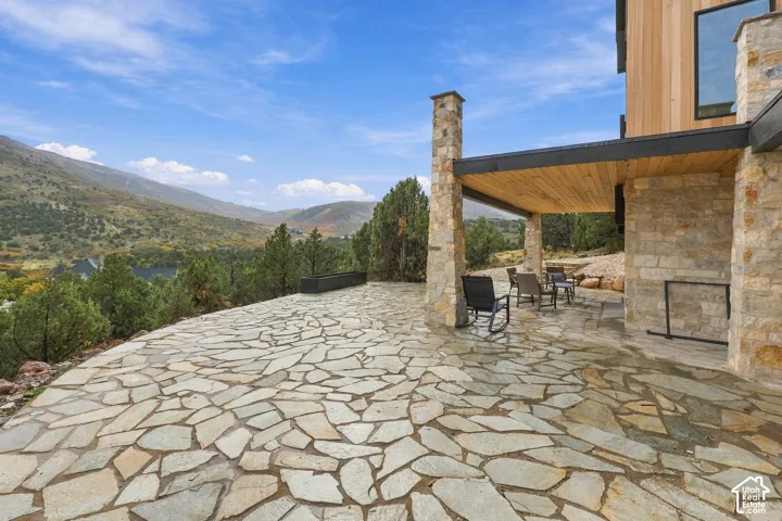 Expansive stone patio featuring natural stone masonry pillars, a wood-paneled ceiling, and mountain topography