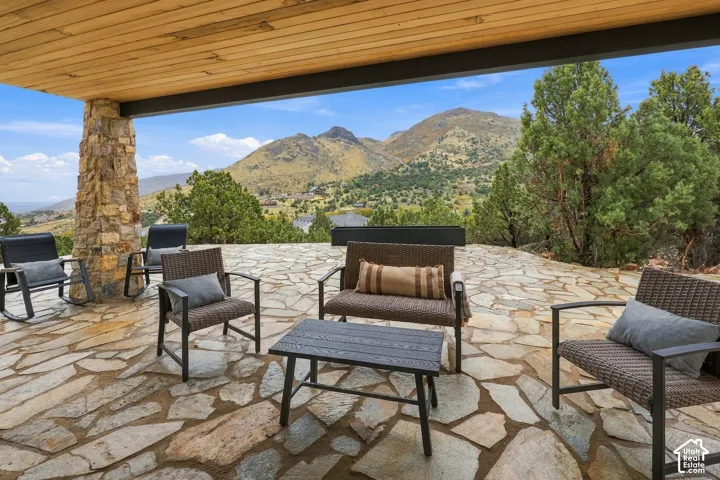 Covered patio featuring a flagstone floor, wood-plank ceiling, and stone-clad support pillar, complemented by a mountain backdrop