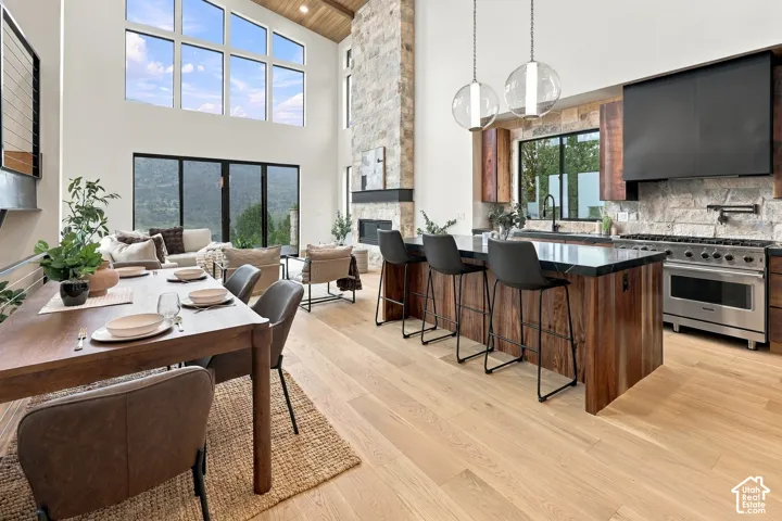 Vaulted ceilings with wood-plank detailing, floor-to-ceiling stone fireplace, large windows, wood-finish flooring, and gourmet kitchen featuring a stone-clad wall and expansive island
