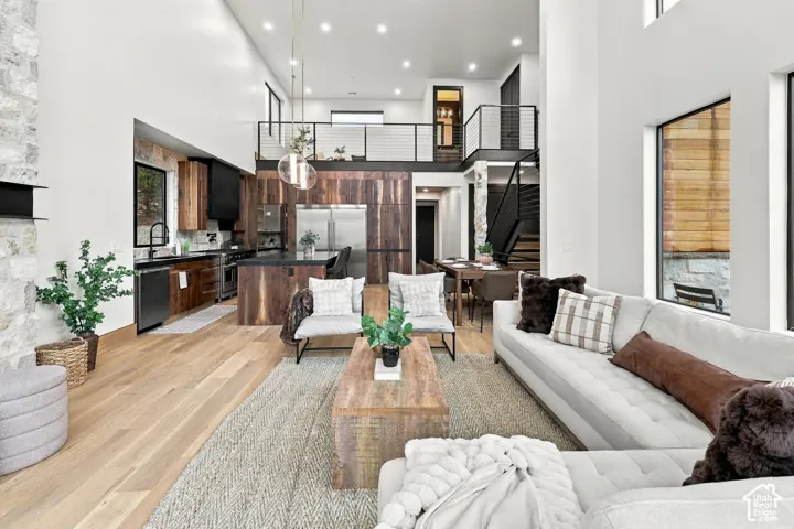 Open-concept interior featuring double-height ceilings, wood-finish flooring, floor-to-ceiling stone fireplace surround, custom wood cabinetry, and a black metal mezzanine railing
