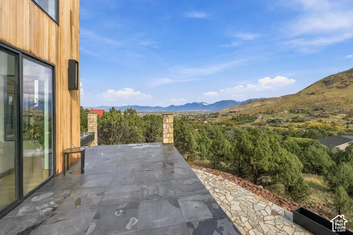 Master bedroom outdoor deck  featuring stone-tiled terrace featuring vertical wood-clad exterior siding, stone-capped pillars, and panoramic mountain backdrop