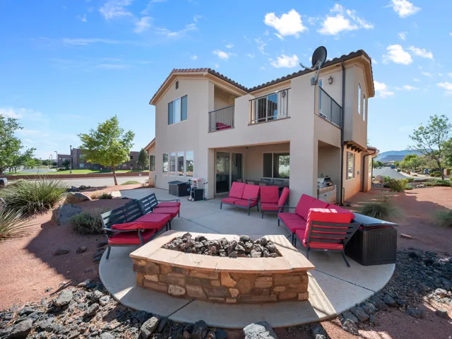 Stone-clad fire pit, concrete patio, built-in outdoor grill station, upper-level balcony with metal railing, and stucco exterior