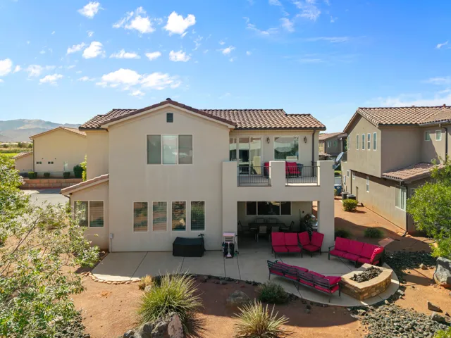 Rear exterior featuring a tiled roof, stucco finish, upper-level balcony, ground-level patio, and a built-in fire pit