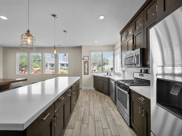Spacious kitchen featuring an extended island with white countertops, dark wood-finish cabinetry, stainless steel appliances, and wood-finish flooring