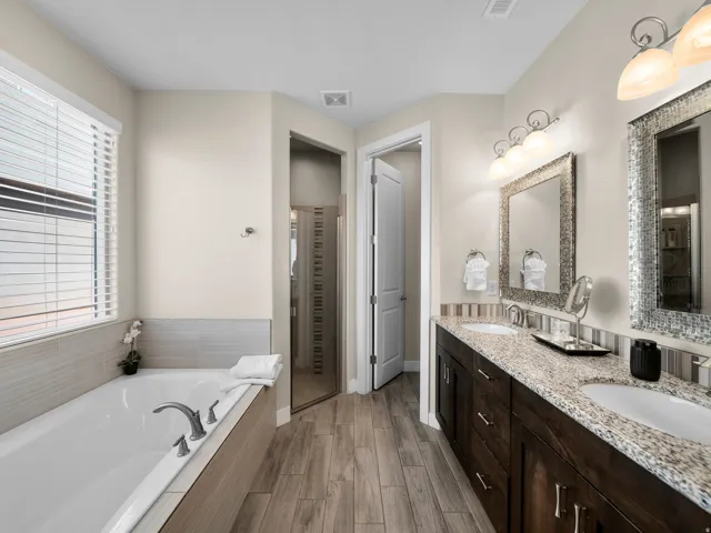 Double vanity with granite countertops, wood-finish flooring, a soaking tub with tile surround, and a glass-enclosed shower