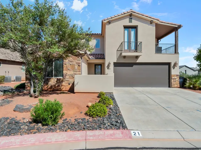 Stucco exterior with stone accents, a private balcony, an attached garage, and desert-style landscaping