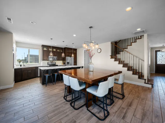 Wood-finish flooring throughout, kitchen with dark wood cabinetry and stainless steel appliances, large kitchen island with countertop seating, staircase with wood treads and wrought iron balusters, and a decorative front door with iron detailing