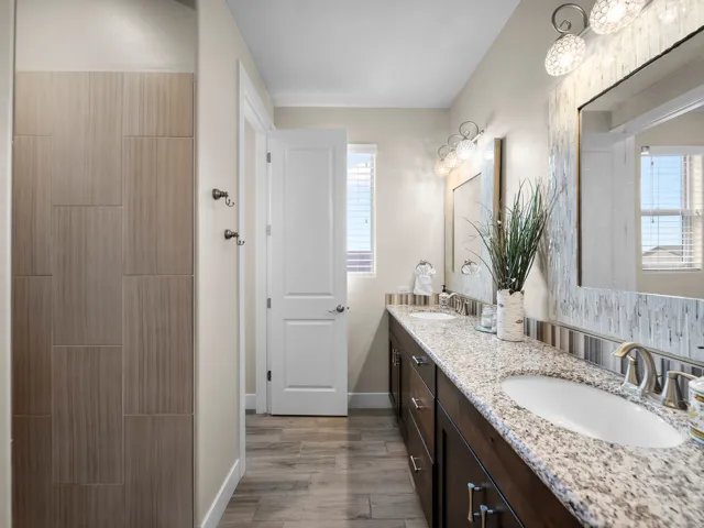 Dual vanity with integrated sinks, granite countertop, rich wood-finish cabinetry, and decorative lighting fixtures