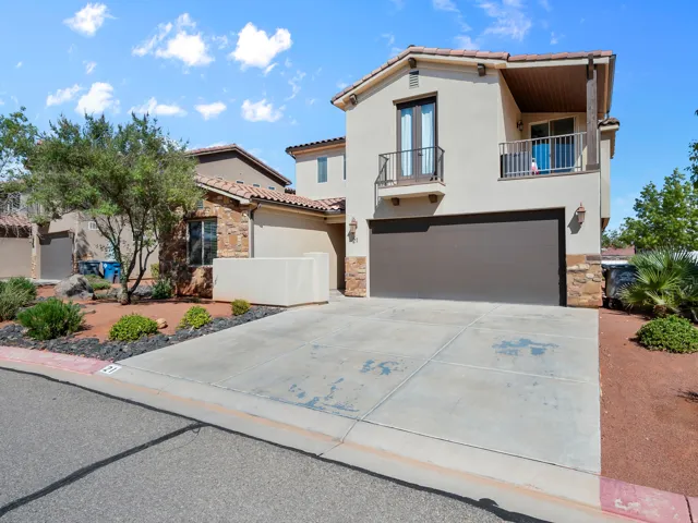 Stucco exterior with stone accents, tile roof, attached garage, and upper-level balcony